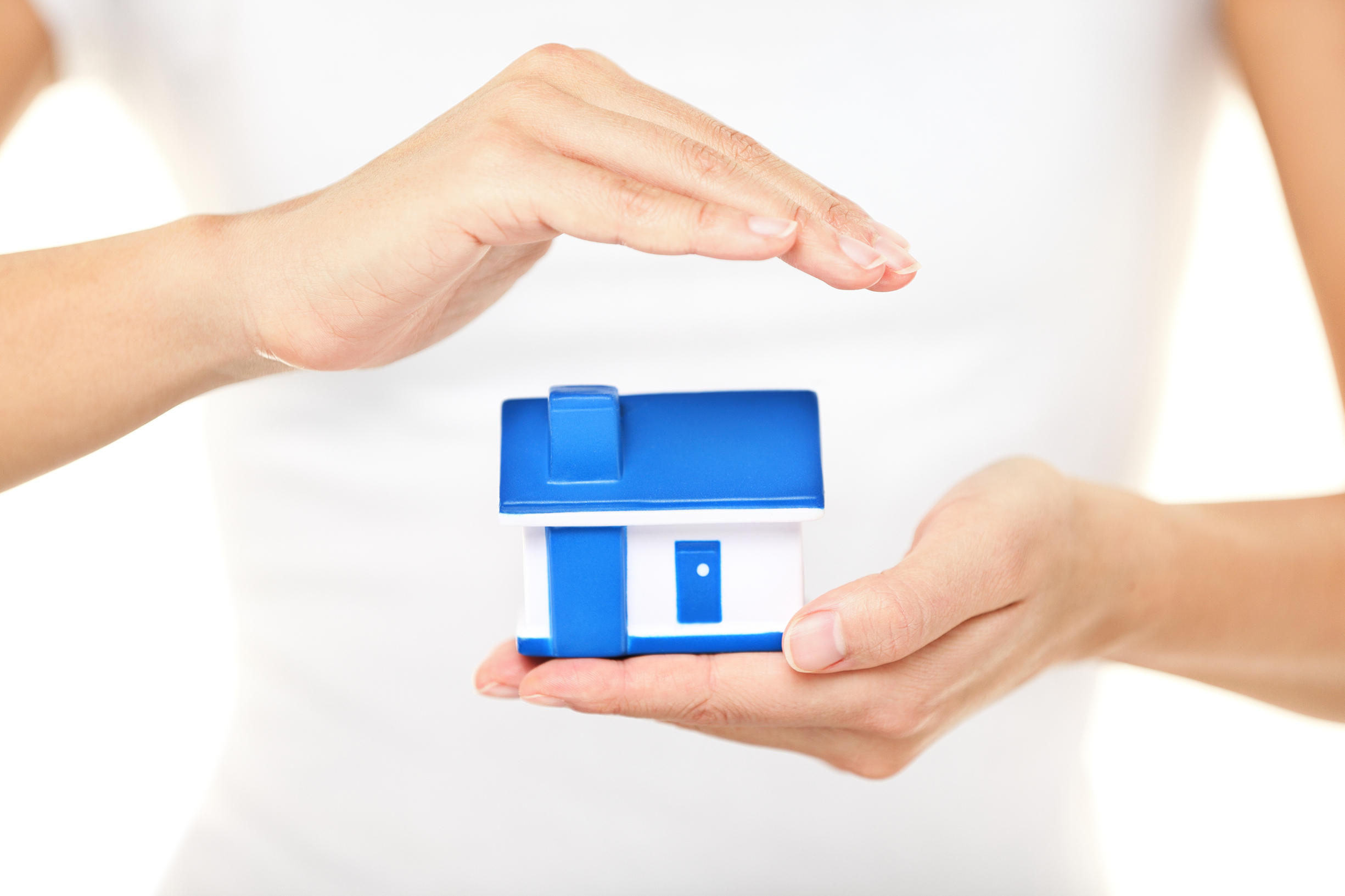 Home insurance. Woman holding a model house in one hand while forming a protective covering with the other conceptual of home insurance and protection